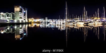 Una vista di varie unità da diporto riflessa in mirror come acqua con edifici di appartamenti visibili sul lungomare. Foto Stock