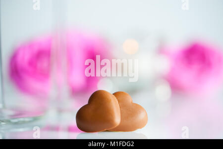 Cuori di cioccolato, rose fiori , due bicchieri di champagne e una candela. sfondo bianco. Il fuoco selettivo. Foto Stock