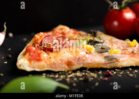 Close up della fetta di italiano Capriciosa pizza di ardesia scura con un pizzicone di origano essiccato Foto Stock