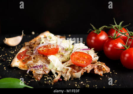 Slace di kebap pizza fatta con carne macinata, cavolo, pomodoro e origano essiccato su ardesia scura Foto Stock