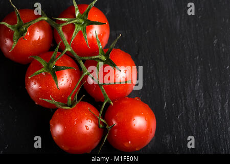 Grappolo di pomodorini con gocce di acqua su di ardesia scura sullo sfondo Foto Stock