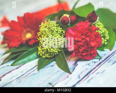 Un mazzo di fiori di colore rosso e verde fiori giacente su di un bluastro tavola in legno rustico sparato contro soft-focalizzata sullo sfondo. Foto Stock