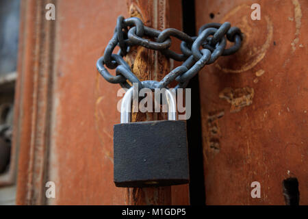 Lucchetto con catena vietato l'ingresso. Legno marrone pelato porta per sfondo. Closeup, dettaglio Foto Stock