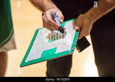 Coach di pallacanestro con appunti e un marcatore di spiegare con lo schema della strategia del gioco per un giocatore. Foto Stock