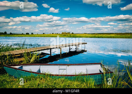 Legno molo sul fiume con una barca da pesca sulla riva del fiume. Paesaggio. Nessuno Foto Stock
