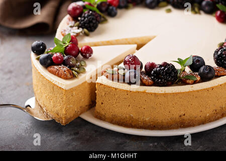 Cheesecake alla zucca con panna acida topping e freschi frutti di bosco stagionali e i dadi con una fetta presa out Foto Stock