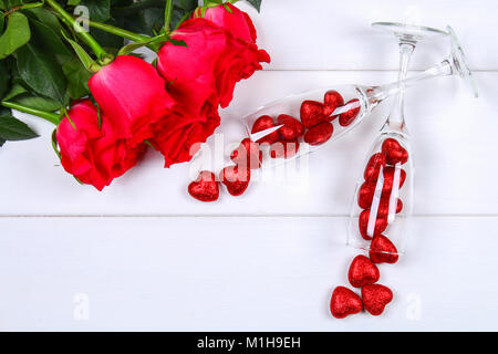 Champagne bicchieri riempiti con un cuore circondato da rose rosse su un bianco tavolo di legno. Modello per il giorno di San Valentino Foto Stock