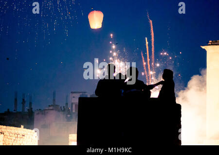 Silhouette di persone in piedi su un tetto con fuochi d'artificio e cielo lanterne in background. Girato durante il festival indiano di makar sankranti o uttaryan in India Foto Stock