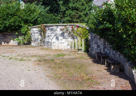 Il muro di pietra nel giardino è coperto con rose rampicanti. Ci sono due panche in ombra. Foto Stock