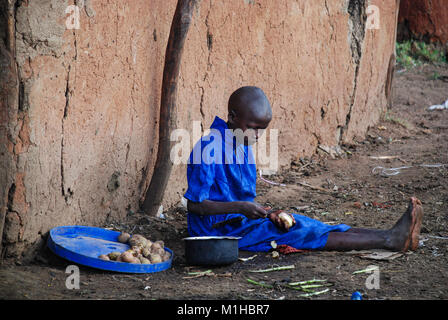 Masai Mara National Park, Kenya 4 Novembre 2008.Child pelare una patata nella parte anteriore della tradizionale casa Masai. Foto Stock