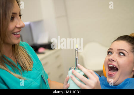 Una giovane donna seduta sulla poltrona del dentista spaventati, lei tiene il dentista la mano non consentendogli di dare il suo anestesia.Lei ottiene il terrore. Foto Stock