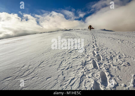 Ampia vista sulla collina innevate con impronte e lontano gli escursionisti a piedi fino con zaino in montagna. Foto Stock