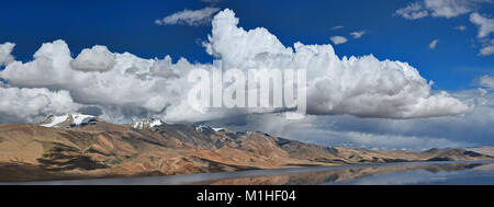 Lago di montagna tra i arancio brillante colline rocciose, nel cielo blu bianchi enormi cumuli di nuvole, Himalaya, photo panorama. Foto Stock