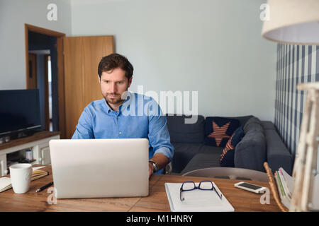 Giovane uomo che lavora da casa su un computer portatile Foto Stock