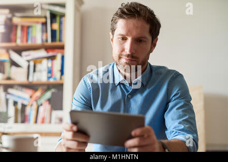 Giovane uomo che lavora da casa utilizzando una tavoletta digitale Foto Stock