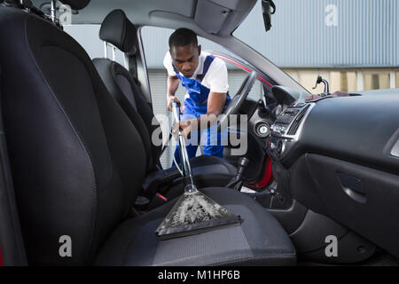 Giovani tuttofare aspirare auto sedile anteriore con un aspirapolvere Foto Stock