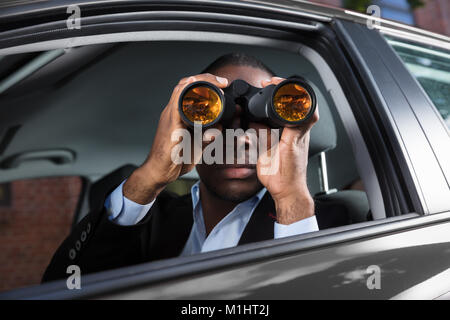 Close-up di un Africano uomo seduto all'interno dell'auto, guardando attraverso il binocolo Foto Stock