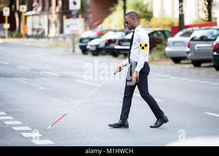 Giovane africano cieco bracciale da indossare a piedi con bastone strada di attraversamento Foto Stock