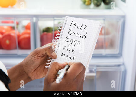 Close-up di giovane donna africana di scrittura elenco dello shopping vicino al frigorifero aperto Foto Stock