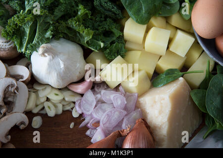 Gli ingredienti freschi con parmigiano, scalogno, aglio, funghi, patate e cavolo riccio. Foto Stock