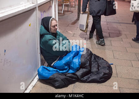 Un senzatetto donna seduta nelle strade di Bristol avvolto in un blu sacco a pelo Foto Stock