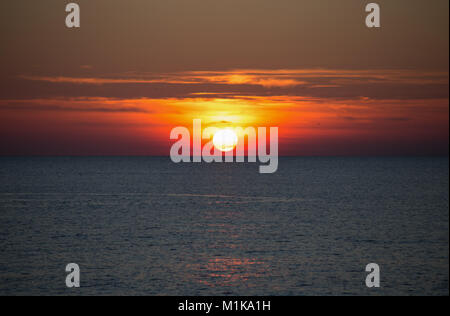 Un bel sole tramontare all'orizzonte sul mare Foto Stock