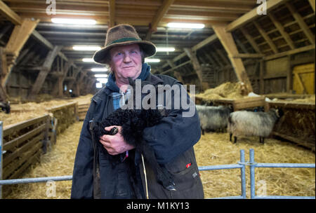 Il pastore Ralf Bachmann porta un agnello che è solo un paio di giorni nella riserva naturale di Lueneburg Heath vicino Niederhaverbeck, Germania, 26 gennaio 2018. Foto: Philipp Schulze/dpa Foto Stock