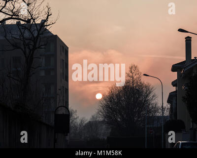 the sun sets behind the buildings on a cold winter afternoon, coloring the sky Foto Stock