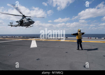 180130-N-NB544-063 Mare delle Filippine (GEN. 30, 2018) di aviazione di Boatswain Mate (manipolazione) 2a classe fede Phillips, dal centro della valle, Kan., segnali per il pilota di un UH-1Y Huey elicottero assegnato al 'Gunfighters' di Marine Attacco leggero elicottero Squadron (HMLA) 369, man mano che si avvicina il ponte di volo dell'assalto anfibio nave USS Bonhomme Richard (LHD 6). Bonhomme Richard sta operando in Indo-Asia-regione del Pacifico come parte di un regolarmente programmata di pattugliamento e fornisce una rapida capacità di risposta in caso di emergenza regionale o calamità naturali. (U.S. Foto di Marina di Massa Comm Foto Stock