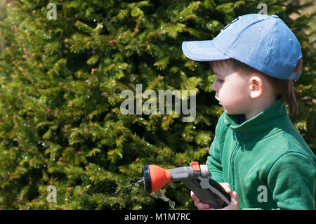 Un bambino, un ragazzo, irrigazione di un tubo flessibile di gomma in un giardino di una casa di campagna, irrigazione Foto Stock