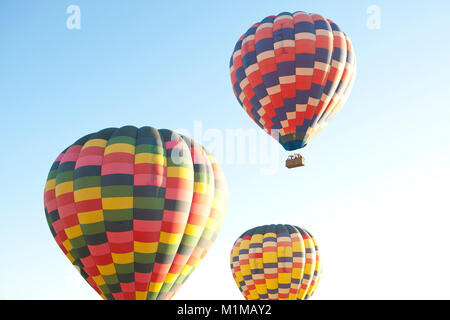 I palloni ad aria calda in volo con colori vibranti contro la mattina presto il cielo blu Foto Stock