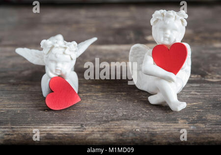 Due angeli di ceramica tenere cuori rossi. Essi sono qui seduti su un tavolo di legno Foto Stock