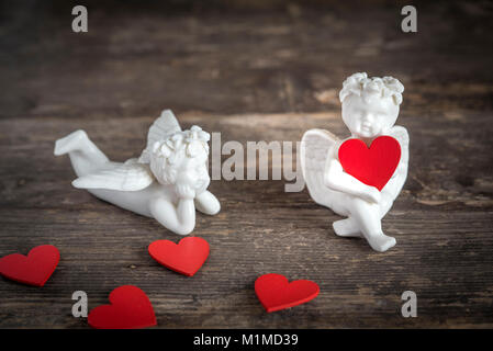 Due angeli di ceramica tenere cuori rossi. Essi sono qui seduti su un tavolo di legno Foto Stock