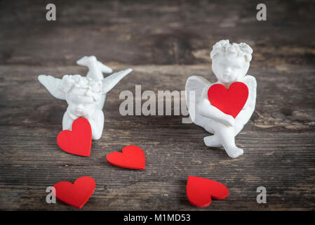 Due angeli di ceramica tenere cuori rossi. Essi sono qui seduti su un tavolo di legno Foto Stock