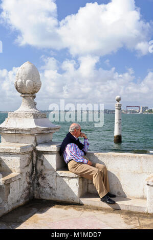 Un vecchio uomo seduto bon un concerto il passo e ammirando la vista sul mare a Lisbona, Portogallo Foto Stock