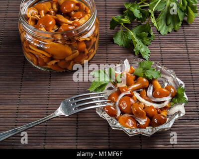 Decapare i funghi in un vaso e in un vaso di vetro condito con cipolla bianca e verde di stand sul tavolo pronti a mangiare Foto Stock