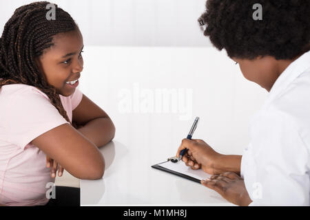 Close-up di sorridente ragazza africana seduti di fronte medico presso la clinica Foto Stock