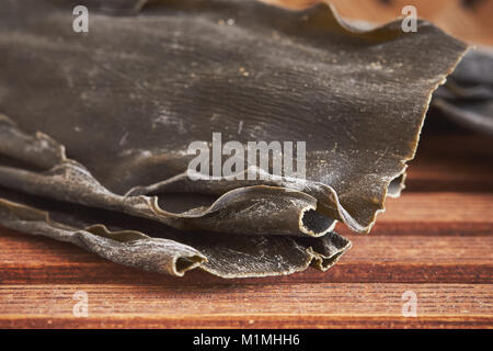 Primo piano della essiccato alghe kombu (Laminariaceae longissima) su sfondo di legno Foto Stock