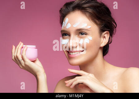 Donna l'applicazione di crema antirughe o anti-invecchiamento della pelle crema di cura. Foto di donna sorridente con pelle sana su sfondo rosa. Cura della Pelle concept Foto Stock