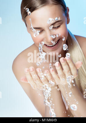 Ritratto di una giovane donna bella pulizia viso con acqua fredda, isolato su sfondo blu, mattina la freschezza, la rimozione di trucco, la salute di un Foto Stock