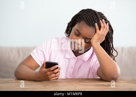 Close-up di un africano ragazza annoiati guardando al telefono cellulare Foto Stock