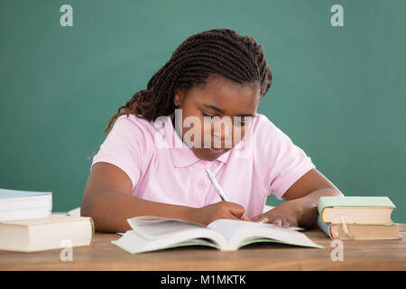 Close-up di una giovane ragazza africana di fare studiare in Aula contro la lavagna Foto Stock
