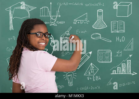 Close-up della ragazza sorridente disegno simboli educativo con il gesso sulla lavagna verde Foto Stock