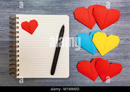 Blocco note con multi-colored hearts e una penna giaceva su un tavolo. Blocco note con il cuore. Foto Stock