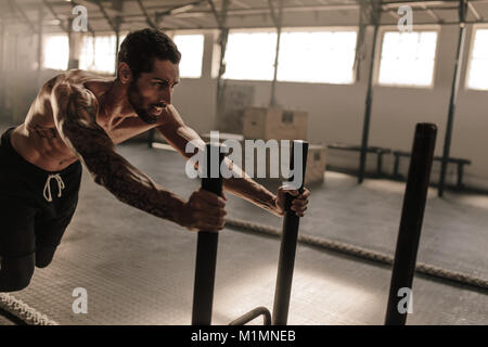 Uomo slitta di spinta nel cross training gym. Uomo muscolare facendo addestramento fisico al club benessere. Foto Stock