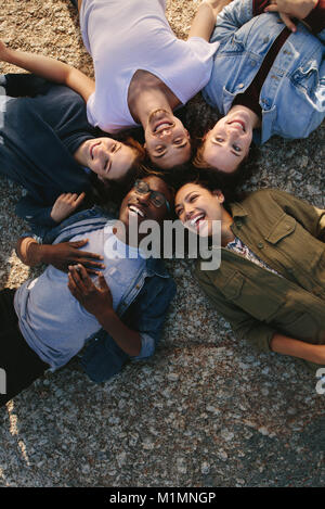 Gruppo di diversi amici che giace a terra nel cerchio esterno. Gli uomini e le donne che giace insieme in un cerchio e sorridente. Foto Stock