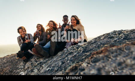 Diversi gruppi di amici avente birre mentre seduto sulla cima della montagna. Allegro giovani uomini e donne godendo e feste all'aperto. Foto Stock