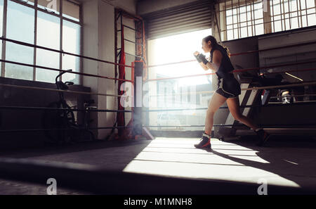 Boxer femmina facendo shadow boxing all'interno di un anello di inscatolamento. Boxer di praticare il pugilato si muove ad un boxing studio. Foto Stock