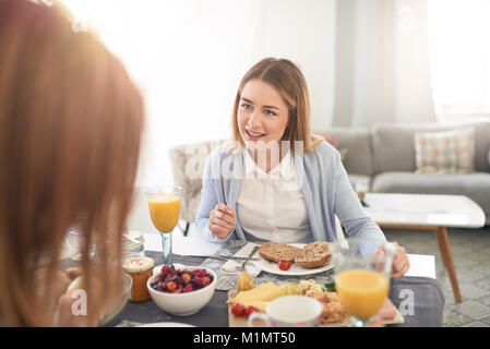 Attraente giovane ragazza seduta in ascolto attento della sua madre come essi godono del tempo di qualità insieme su una sostanziosa prima colazione in un oltre la s Foto Stock