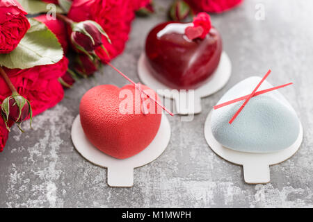 Il giorno di San Valentino o compleanno biglietto di auguri. Partita un dessert nella forma di un cuore rosso. Rose rosse e dessert su vintage tavolo in legno Foto Stock